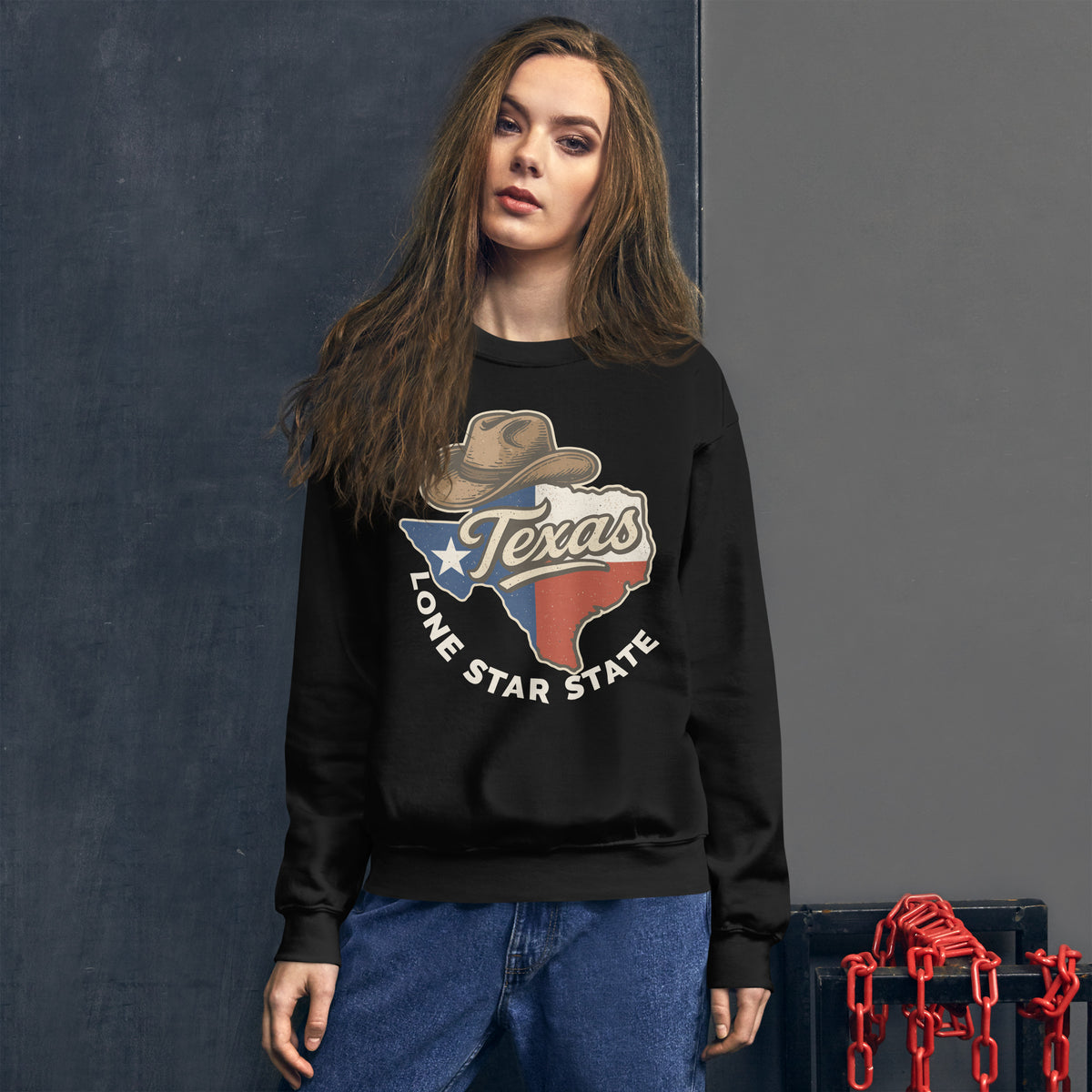 A woman modeling a black crewneck sweatshirt with a 'Texas Lone Star State' graphic on the front, paired with blue jeans, standing against a dark gray textured wall.