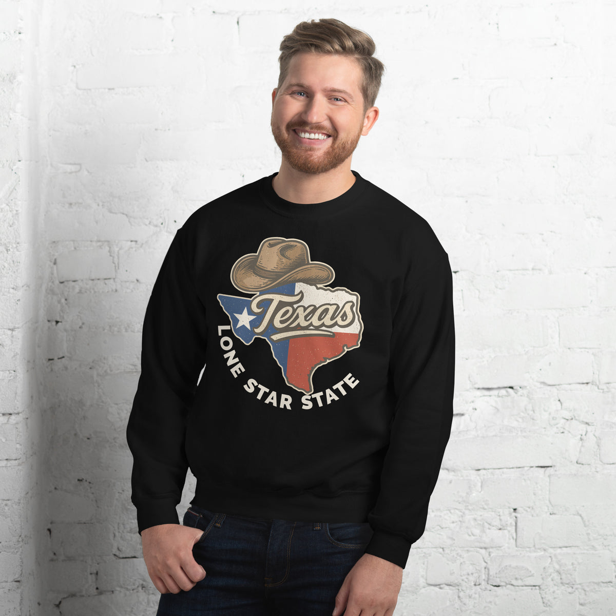 A smiling man wearing a black crewneck sweatshirt with a 'Texas Lone Star State' graphic on the front, standing against a white brick wall.