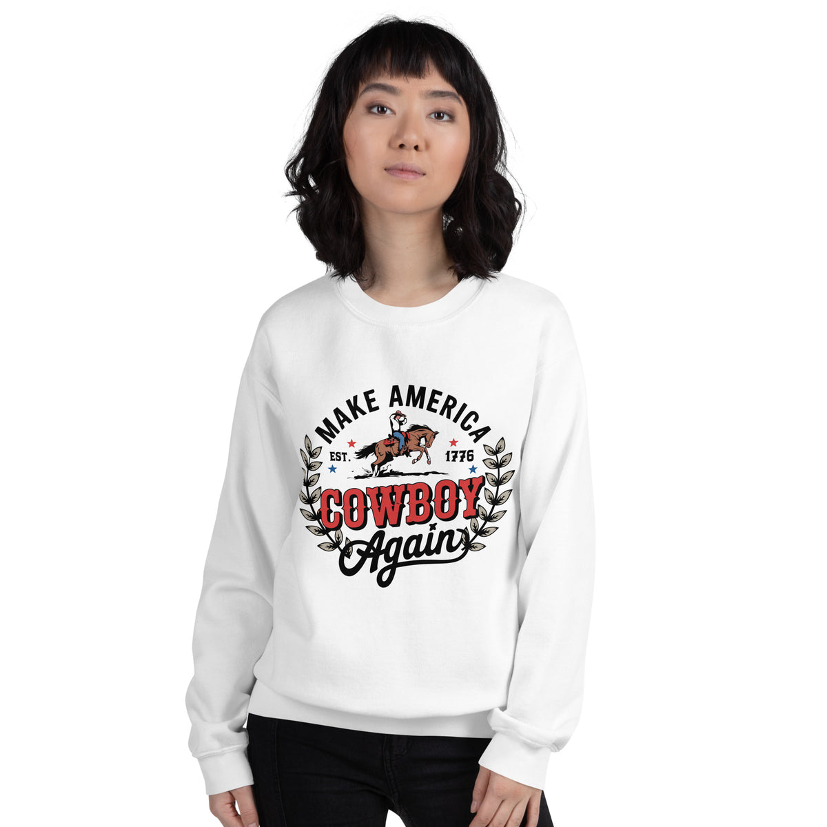A woman wearing a white crewneck sweatshirt with a graphic print that reads 'MAKE AMERICA COWBOY Again' in black and red lettering, featuring an illustration of a cowboy on a horse and a horse rider. The background is solid white.