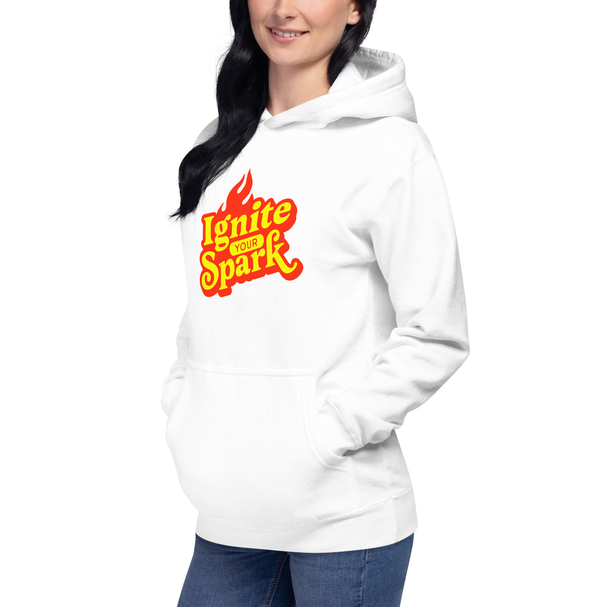 A woman wearing a white pullover hoodie with a 'Ignite Your Spark' flame graphic on the chest, paired with blue jeans, shown against a plain white background.