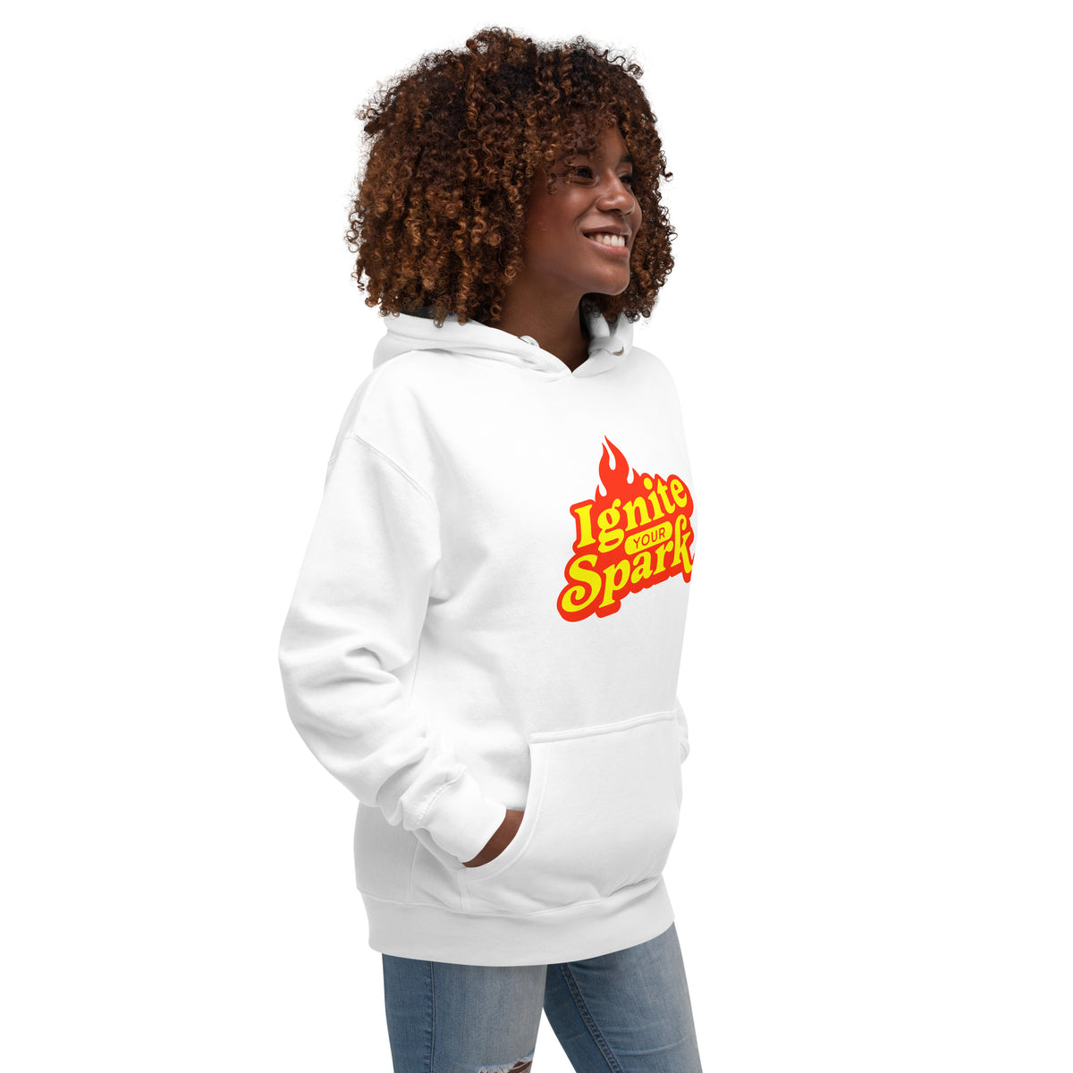 A woman with curly brown hair wearing a white pullover hoodie with a red and yellow flame graphic that reads 'Ignite Your Spark' on the chest, paired with blue jeans, set against a plain white background.