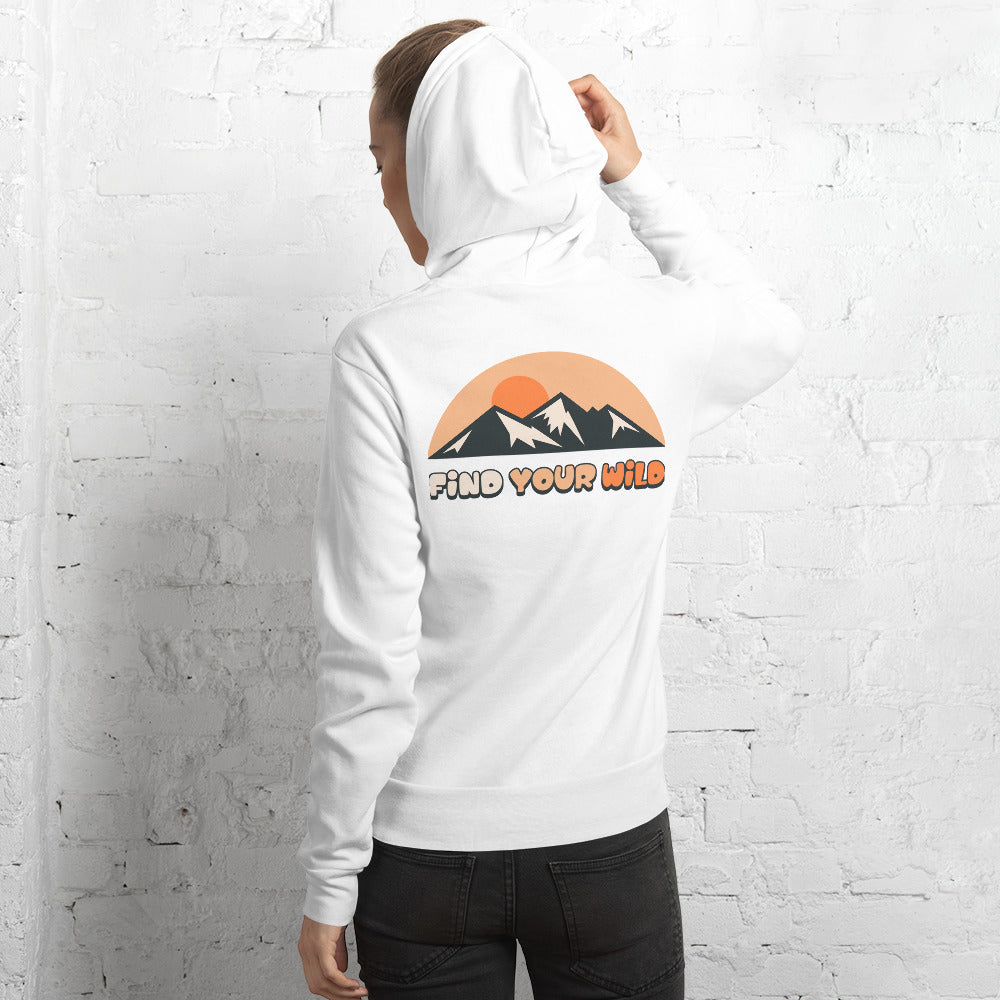 A person wearing a white hoodie, shown from the back, standing against a white brick wall. The hoodie features a graphic of a mountain range under a retro orange sunset with the text 'FIND YOUR WILD'.
