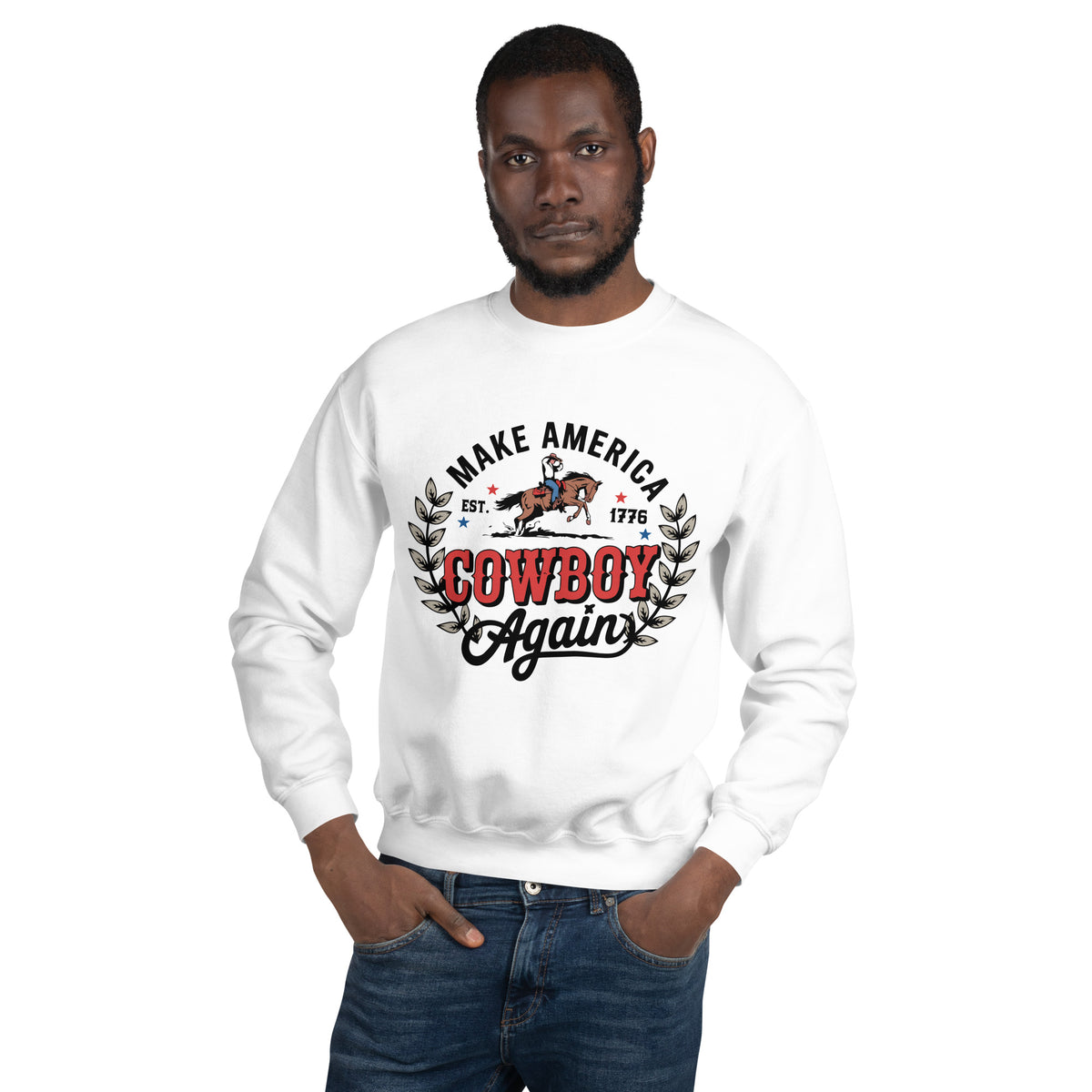 A man wearing a white crewneck sweatshirt with a graphic print that reads 'MAKE AMERICA COWBOY Again' with a cowboy riding a bucking horse, paired with blue jeans, against a plain white background.