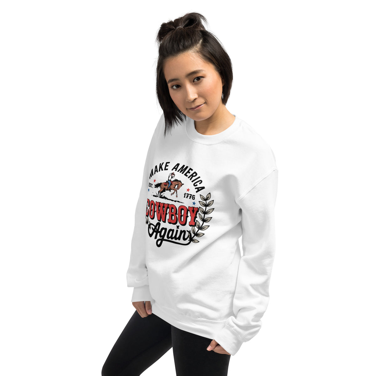 A woman modeling a white long-sleeve crewneck sweatshirt with a graphic print that reads 'MAKE AMERICA COWBOY AGAIN' with a cowboy illustration, against a plain white background.