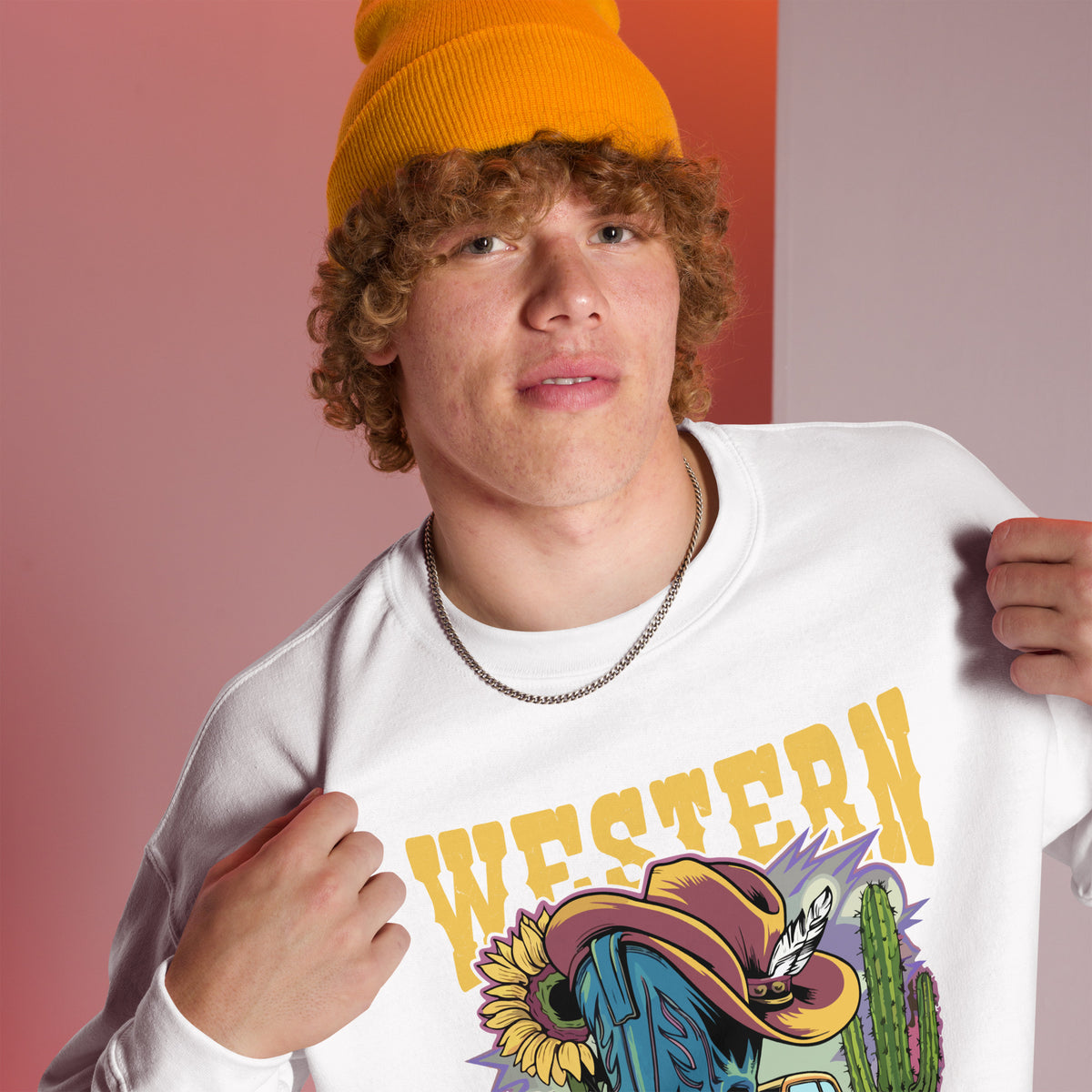 A young man wearing a bright yellow beanie and a white graphic sweatshirt with a colorful 'WESTERN' print, posed against a pink and orange studio background.