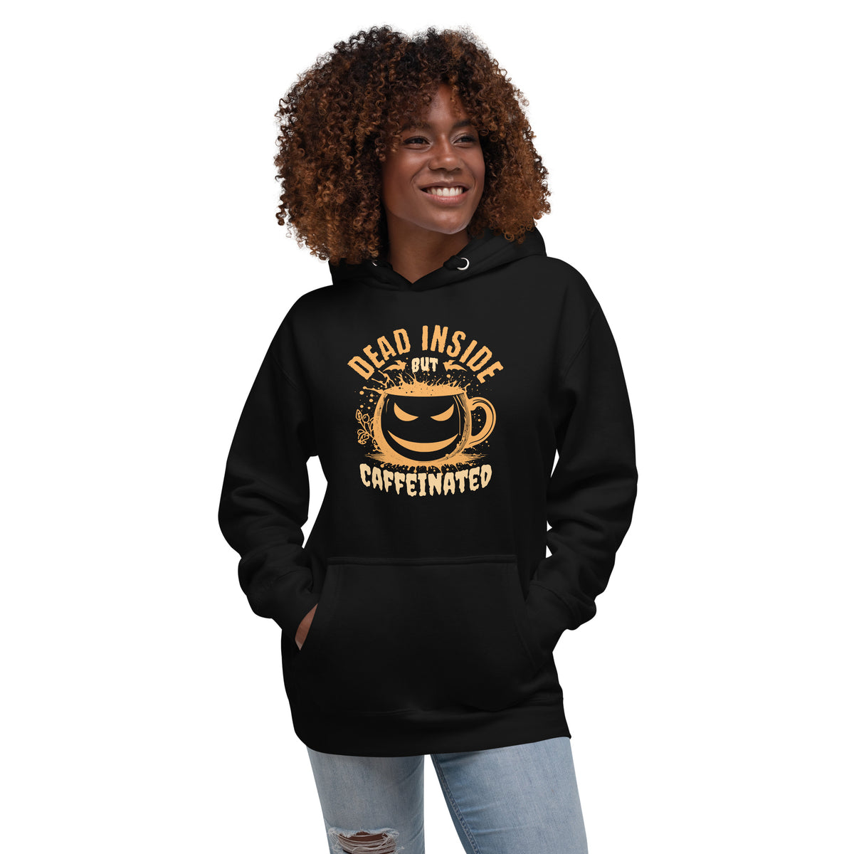 A woman with curly brown hair wearing a black pullover hoodie with a gold graphic that reads 'DEAD INSIDE BUT CAFFEINATED' around a coffee cup illustration, paired with light blue jeans, on a plain white background.