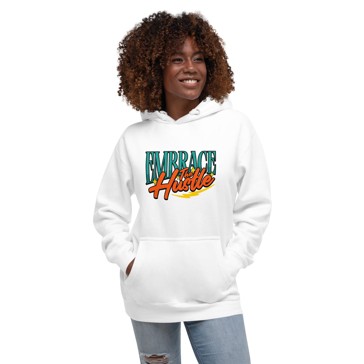 A woman with curly brown hair wearing a white pullover hoodie with a colorful retro-style graphic that reads 'EMBRACE HUSTLE' in teal and orange, paired with light blue jeans, against a plain white background.