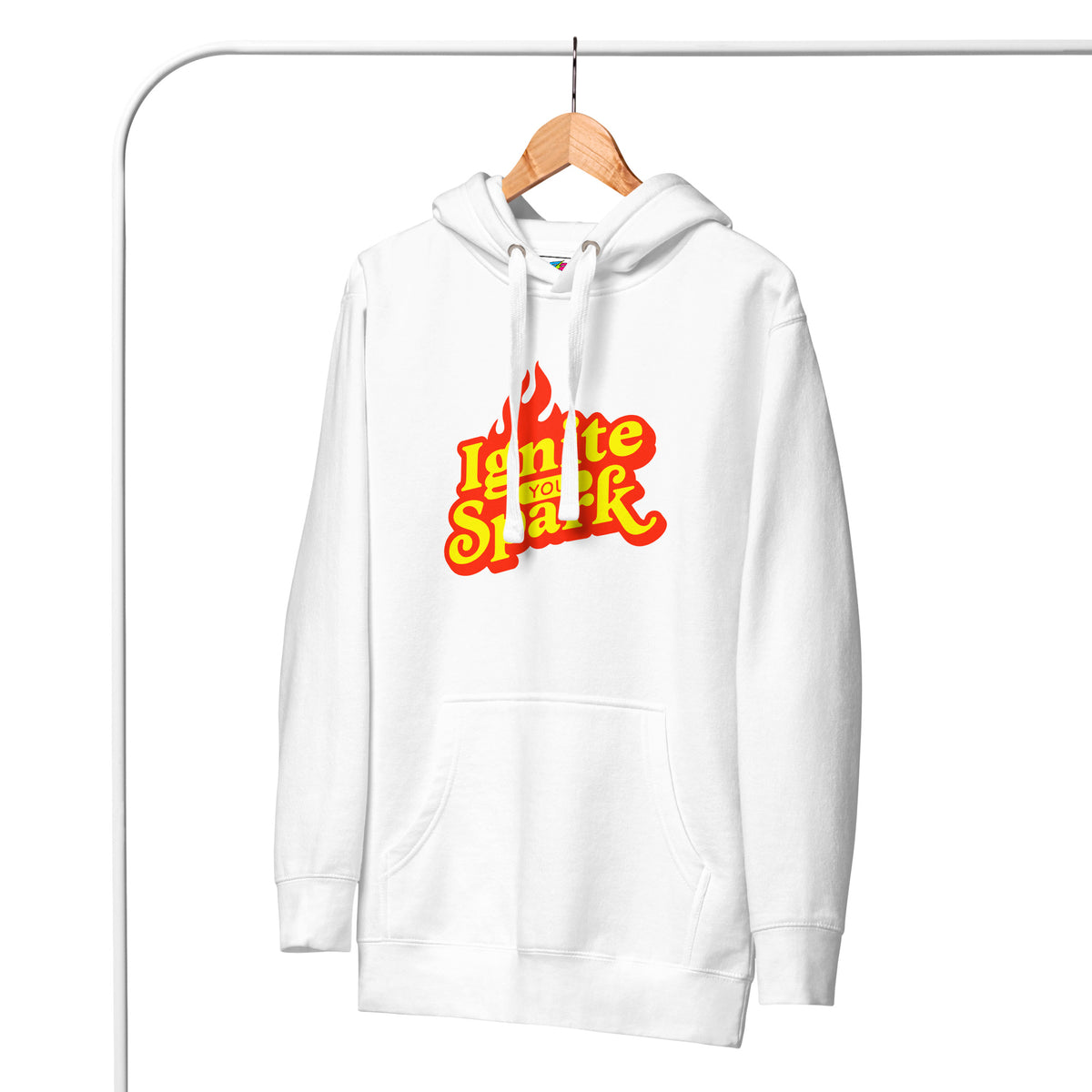 A white pullover hoodie hanging on a wooden hanger against a white background, featuring a 'Ignite Your Spark' flame graphic in red and yellow on the chest.