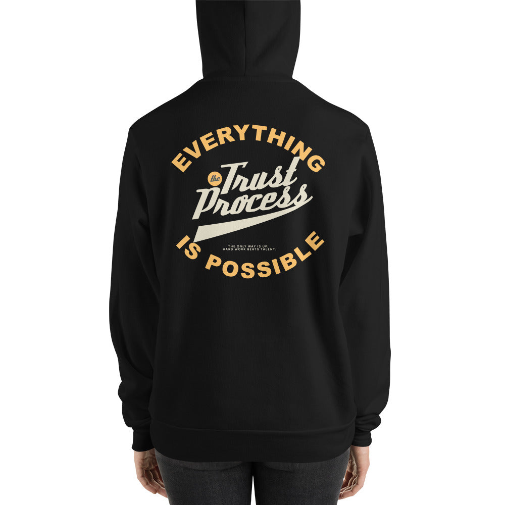 A person shown from the back wearing a black hoodie with a large back graphic that reads “Everything Trust Process Is Possible” in cream and gold lettering.