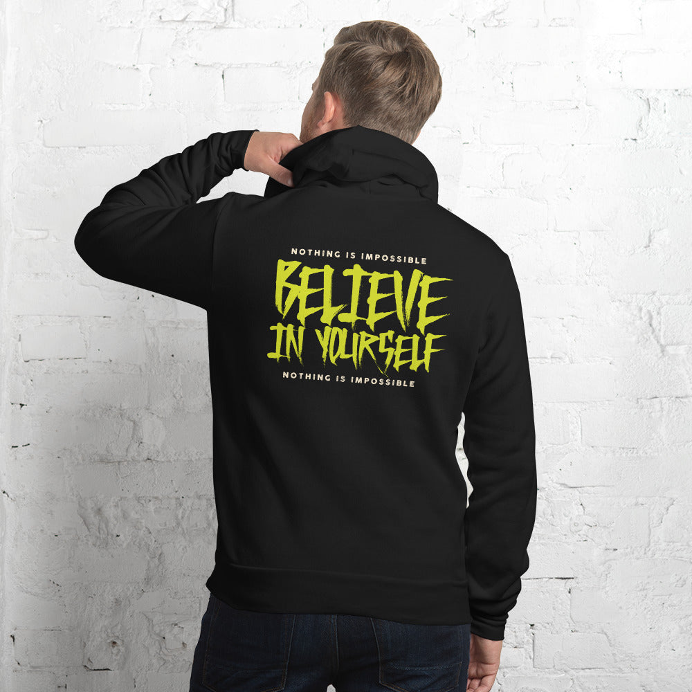 A man viewed from behind wearing a black hoodie with a large golden-brown dripping swirl graphic printed on the back, standing against a white brick wall.