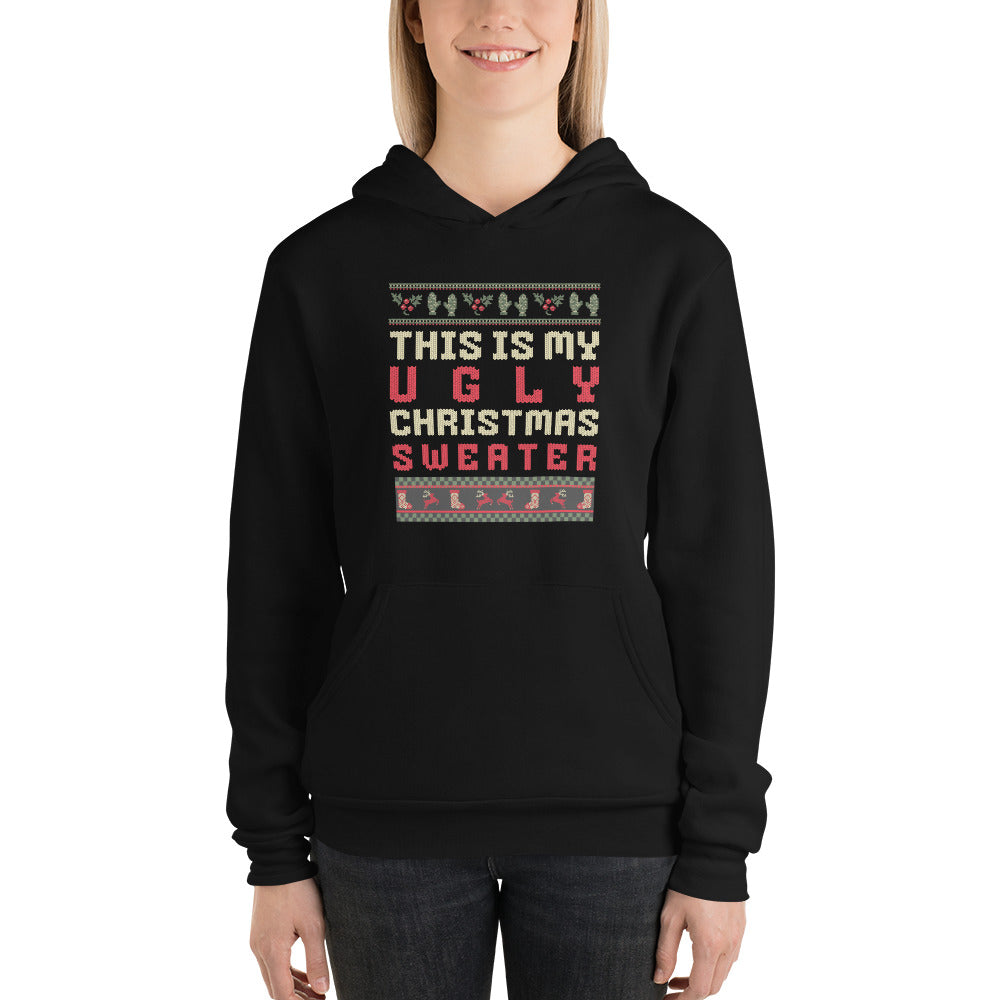 A woman wearing a black pullover hoodie with a festive graphic that reads 'THIS IS MY UGLY CHRISTMAS SWEATER' in red, white, and gray text, framed by holiday-themed borders. The photo is shot against a clean white background.