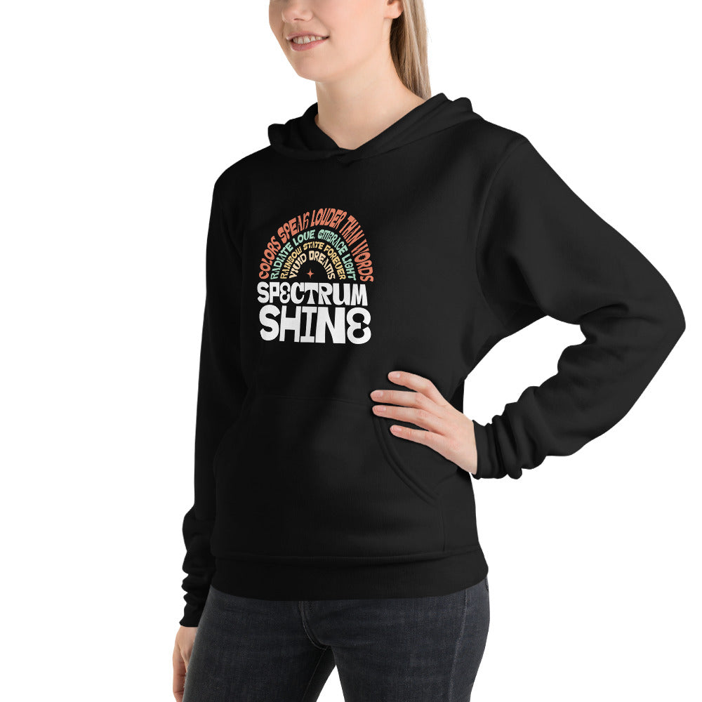 A woman wearing a black pullover hoodie with a colorful rainbow graphic and the text 'SPECTRUM SHINE' on the chest, paired with dark gray jeans, against a plain white background.