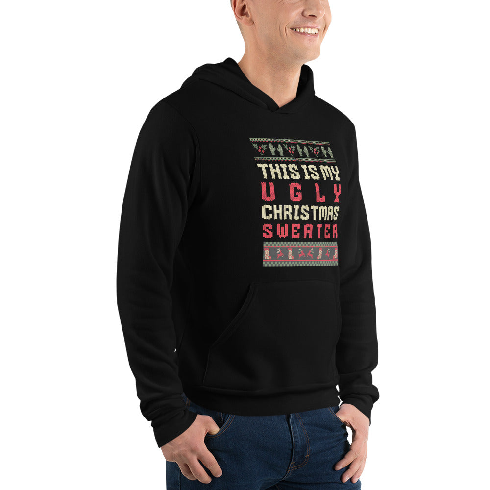 A man wearing a black pullover hoodie with a festive graphic that reads 'THIS IS MY UGLY CHRISTMAS SWEATER' in red and white text, framed by pixelated borders. The photo is taken against a clean white background.