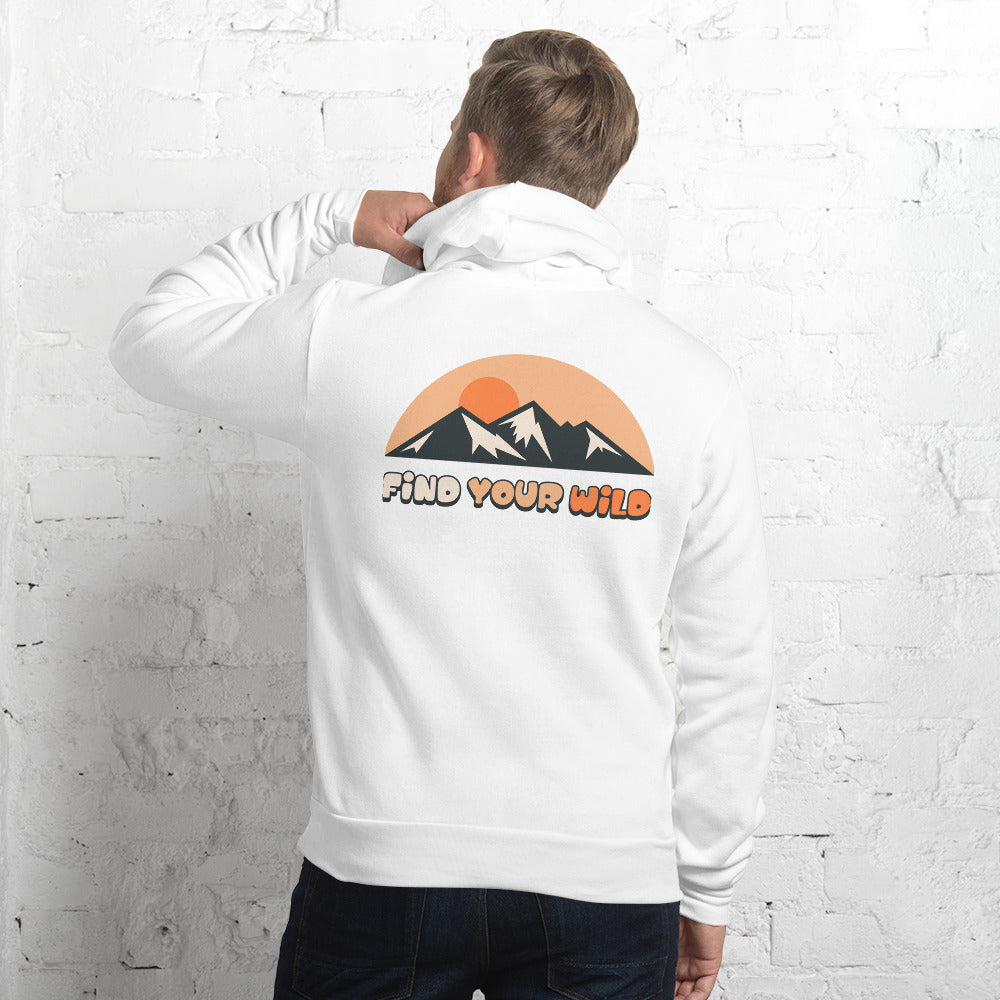 A man wearing a white hoodie with a mountain sunset graphic and the text 'FIND YOUR WILD' on the back, standing against a white brick wall.