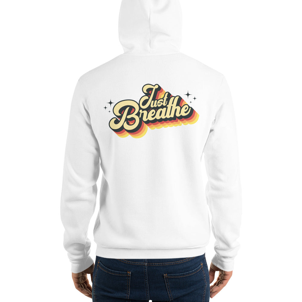 A white pullover hoodie shown from the back, worn by a model. The back of the hoodie features a colorful retro-style graphic that reads 'Just Breathe' in yellow, orange, and dark blue lettering with small star accents.