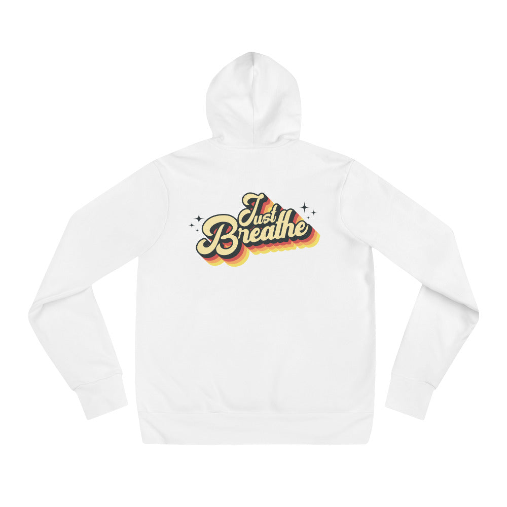 A white long-sleeve hoodie shown flat against a white background, featuring a retro-style graphic on the chest that reads 'Just Breathe' in yellow, orange, and red with small star accents.